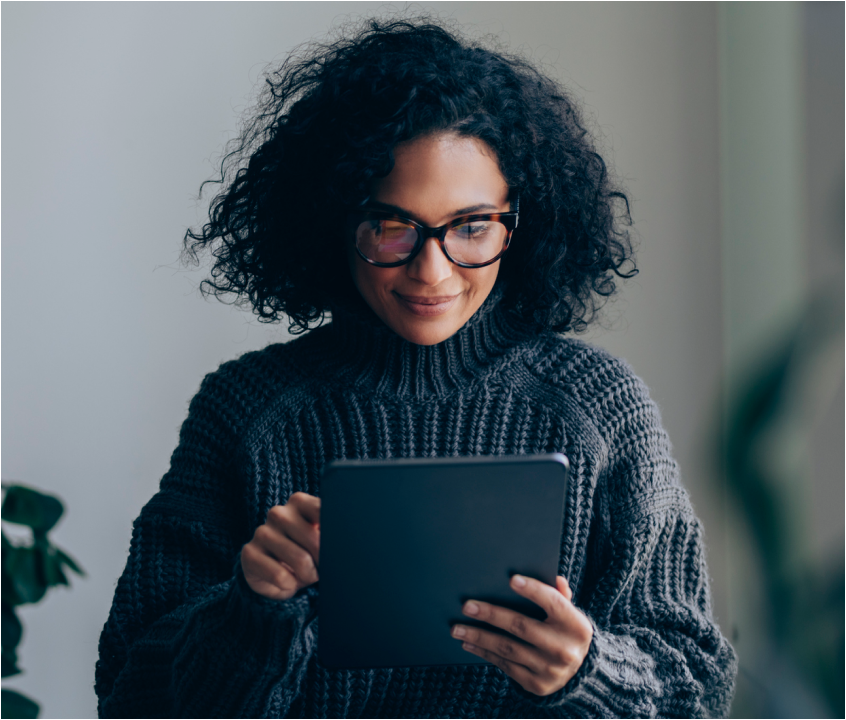 Woman wearing glasses smiling while looking down at the tablet in her hands.