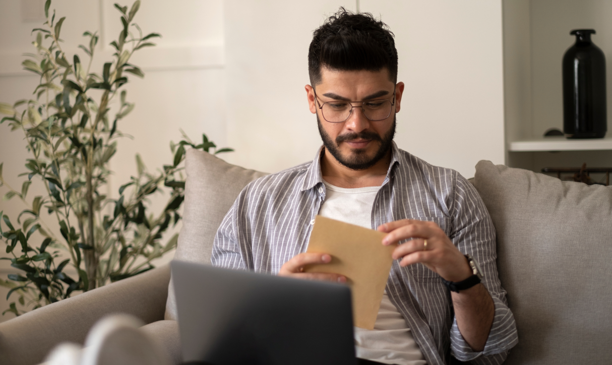 A man looks at mail as he sits on a couch in front of a computer