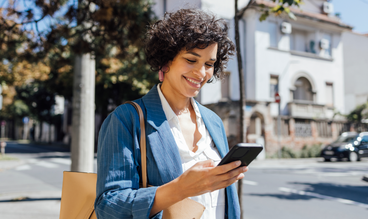 A woman looks at the phone she is holding and smiles as she walks outside