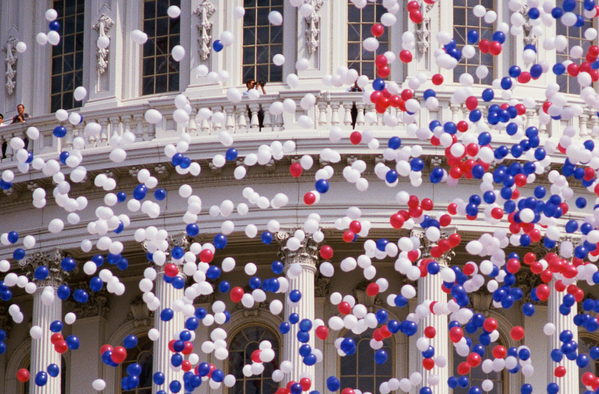 Hundreds of red, white, and blue balloons floating in the air in front of the U.S. Capitol Building dome.