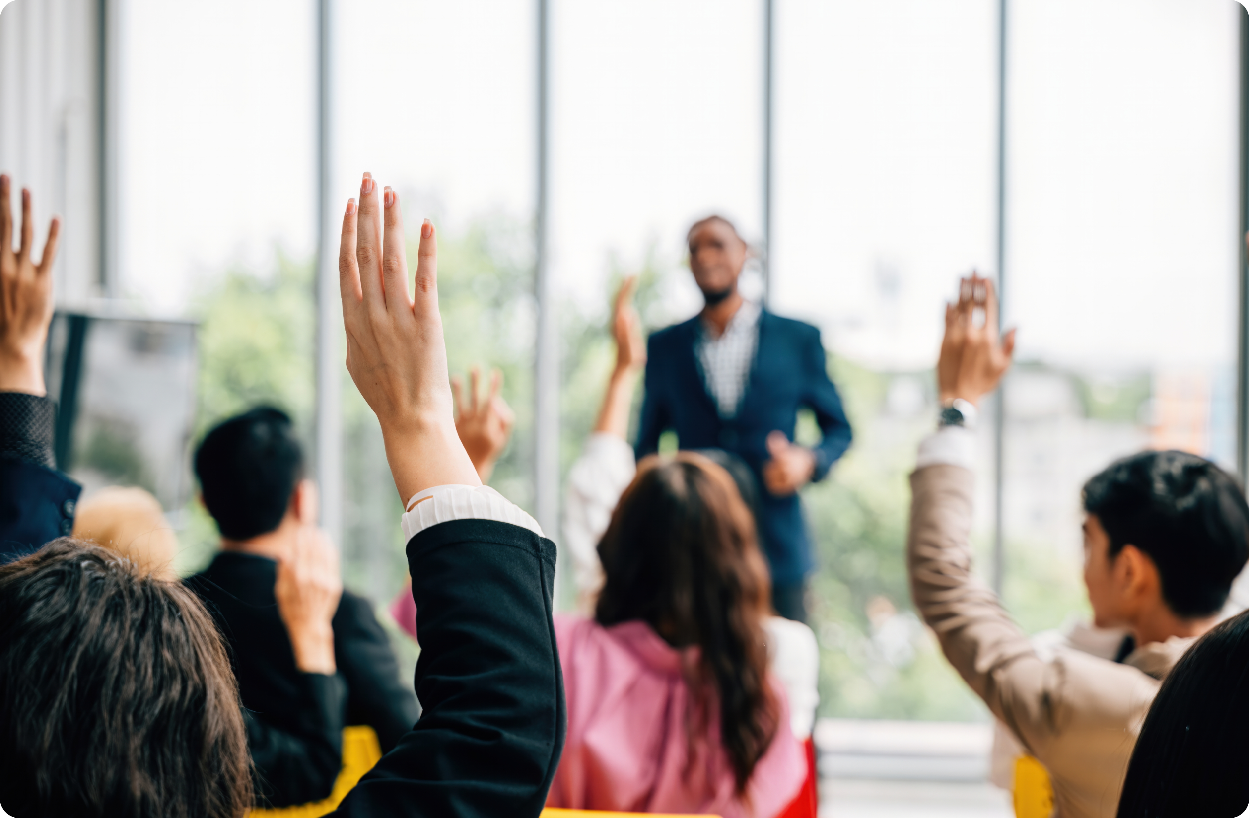 Candidate speaking in front of a group with their hands up to ask questions.