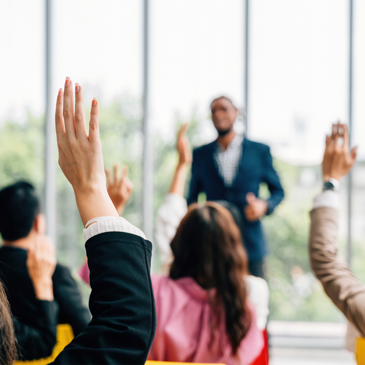 Candidate speaking in front of a group with their hands up to ask questions.
