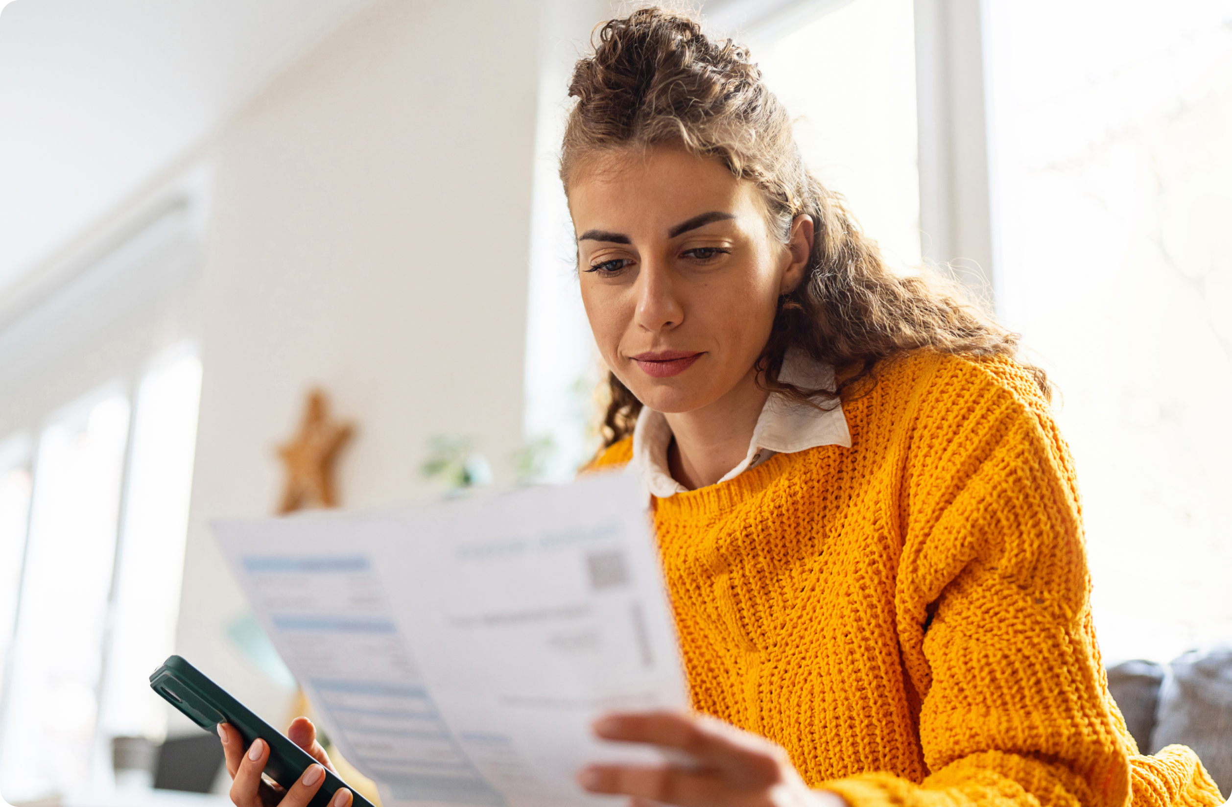 Woman holding her phone in one hand and looking down at a mail piece in the other hand.