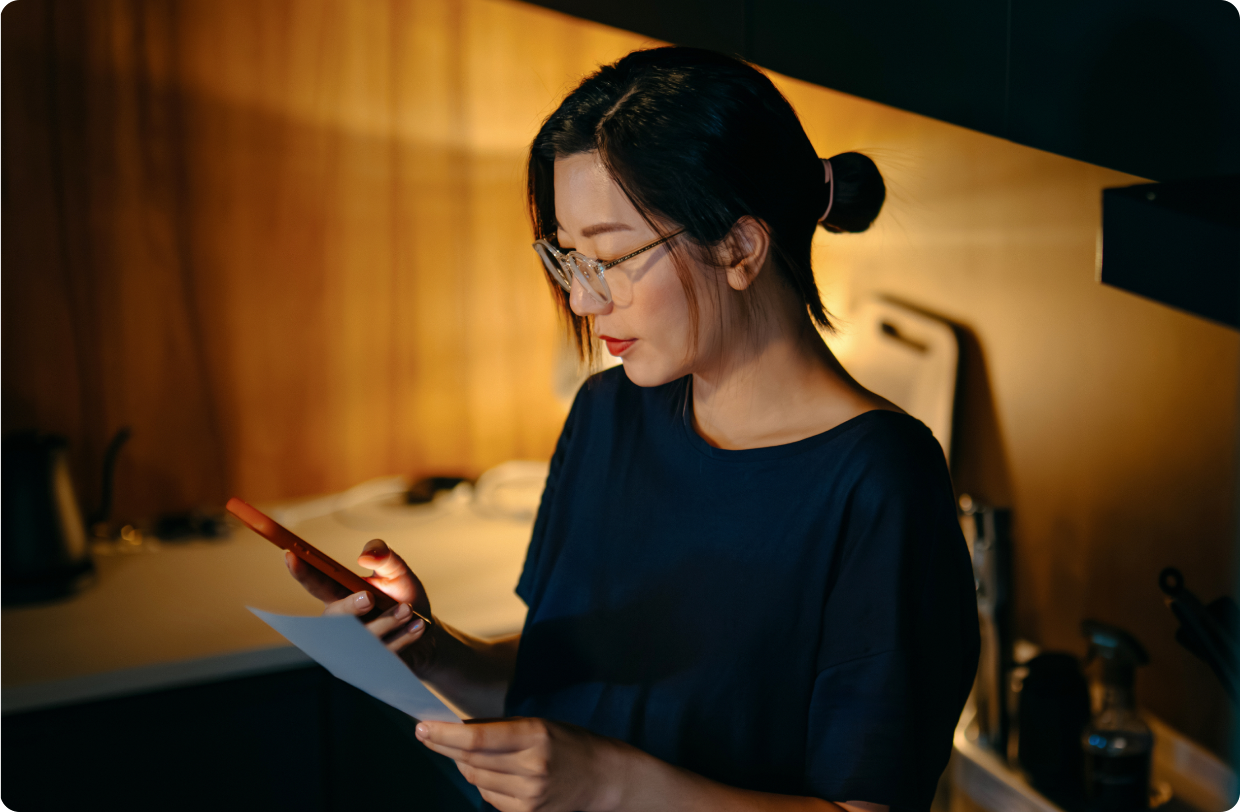 Woman looking down at her phone in one hand while holding a direct mail piece in the other.